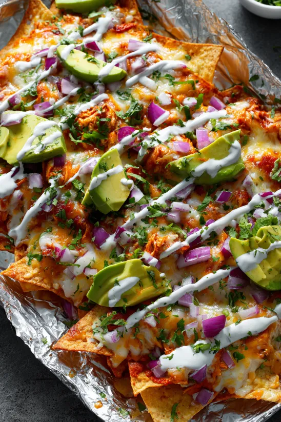 Eine Platte mit Buffalo Chicken Nachos, die mit Avocado, Onion und Mayonnaise garniert sind.