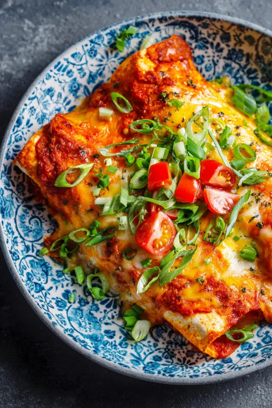 Ein Teller Käse-Enchiladas mit Frühlingszwiebeln oben drauf.