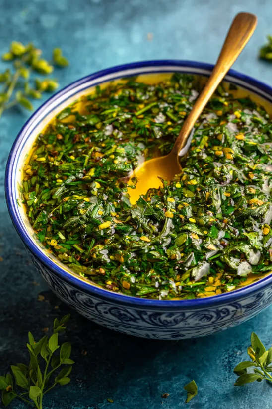 Ein Bogen Holz, der in eine Schüssel gesteckt ist, die mit einer Chimichurri-Zubereitung gefüllt ist.