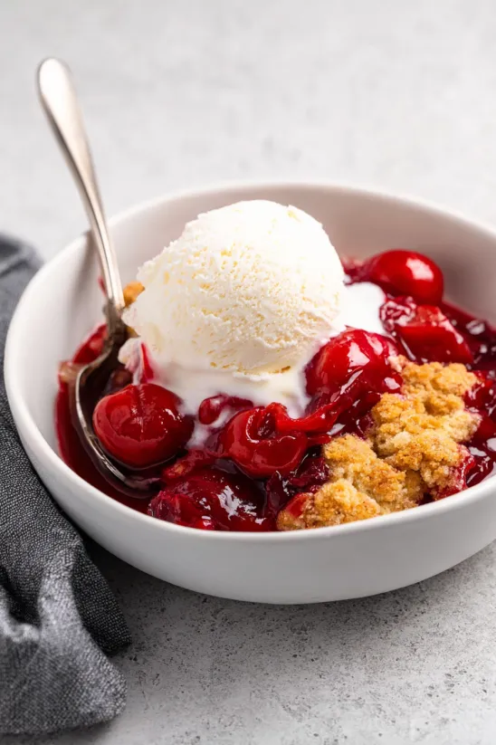 Ein Glas mit Cherry Cobbler, das mit Eis und einer Tasse gereicht wird.