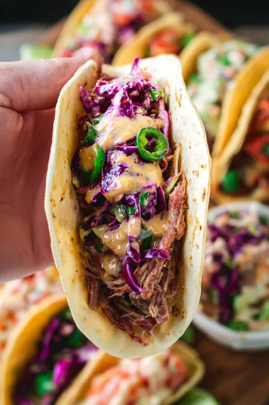 Jemand hält einen Taco mit Fleisch und Kraut in der Hand.