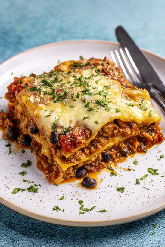 Auf einem Teller liegt Mexikaner-Lasagne, daneben eine Gabel.
