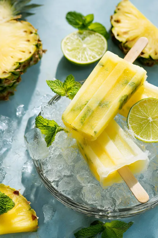 Eine Schale mit Ananas-Eis am Stiel, Limetten und Minze.