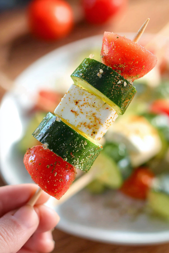 Jemand hält einen Spieß mit Wassermelonen- und Gurkenscheibe darauf.