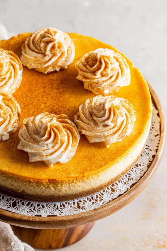 Ein Stück Kürbis Cheesecake mit weiß-brauner Deko obendrauf.