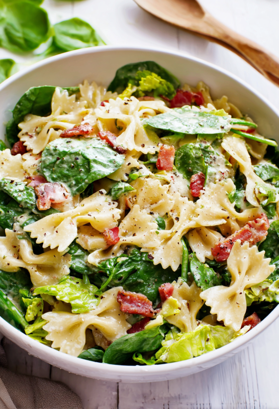 Eine Schüssel mit Nudelsalat, Speck und Spinat.