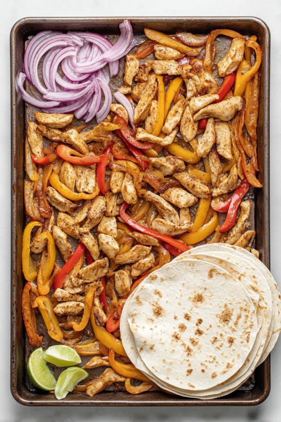 Eine Tafel mit einer Mischung aus Chicken, Paprika, Zwiebeln und anderen Zutaten, die auf einem Blech oder einer Pfanne gegart werden.
