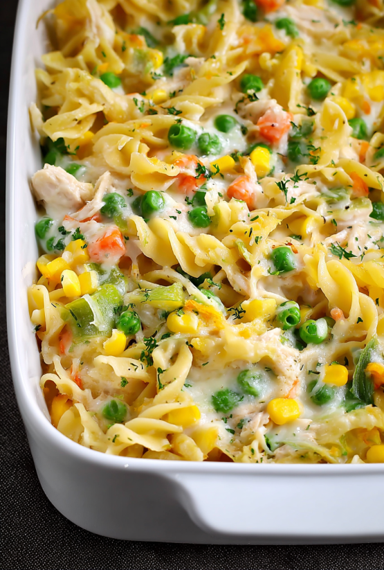 Ein weißer Teller mit einer Chicken Noodle Casserole, die aus macaroni, kartoffeln, peas, carrots und chicken besteht.