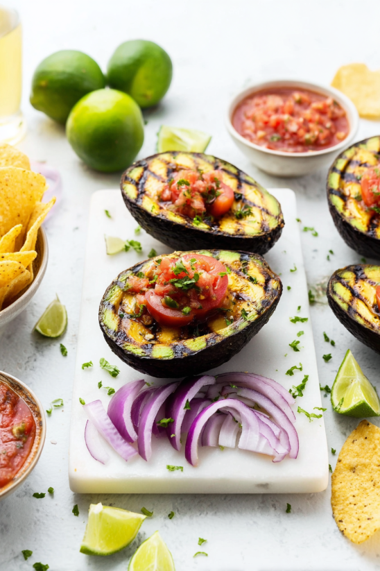 Eine Tafel mit verschiedenen gegrillten Avocados, die mit Pico de Gallo garniert sind.