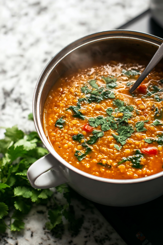 Ein Topf mit einer cremigen, roten Linsen-Gericht, das mit Spinat und Tomaten zubereitet wurde.