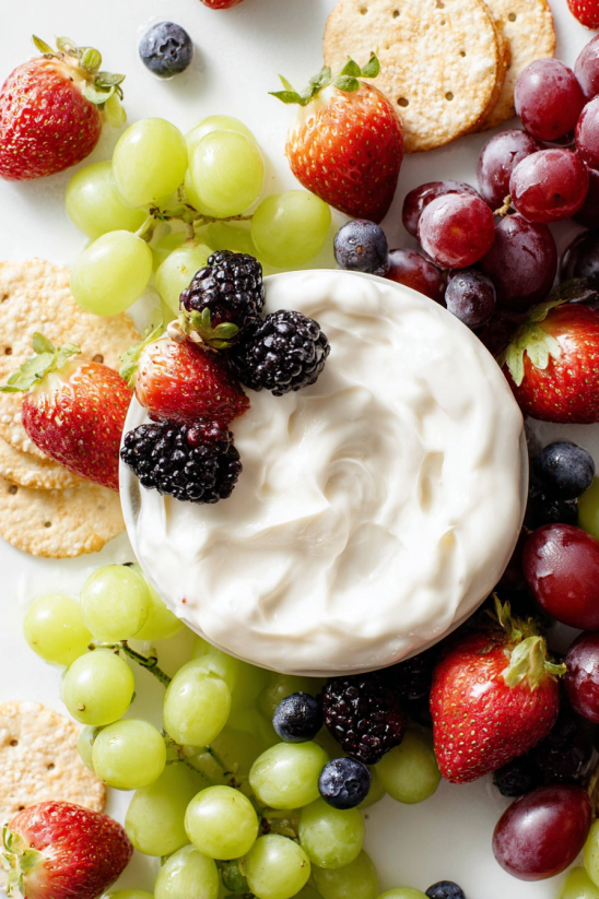 Eine Tasse mit Marshmallow Fruchtsoße, die mit verschiedenen Früchten wie Gurken, Strawberries, Blueberries, Raspberries, Grapes und Granola garniert ist.