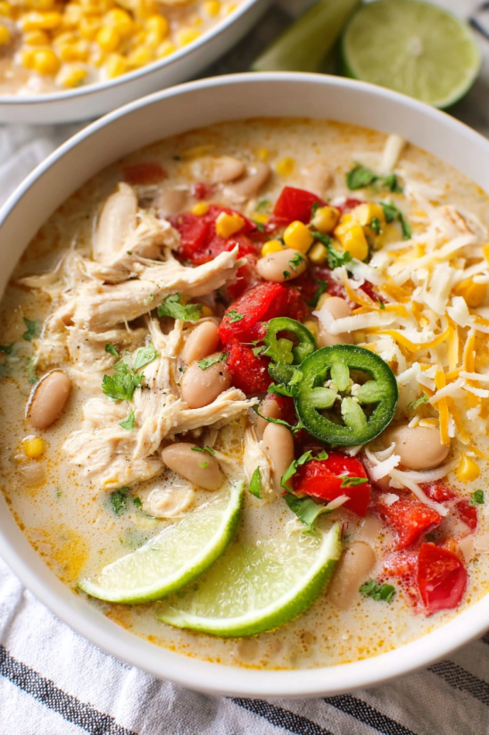 Ein weißer Becher mit einer cremigen weißen Chili, die mit verschiedenen Zutaten wie Kartoffeln, Korn, Tomaten, Paprika, Chili und Zwiebeln zubereitet wurde.