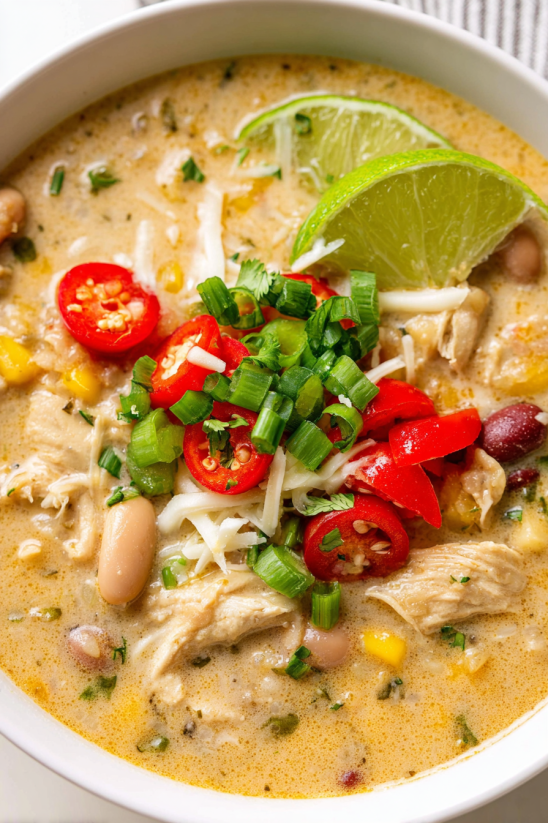 Ein Bild von einer creamy weißen Chili mit verschiedenen Zutaten wie Tomaten, Koriander, Lime und Chili.