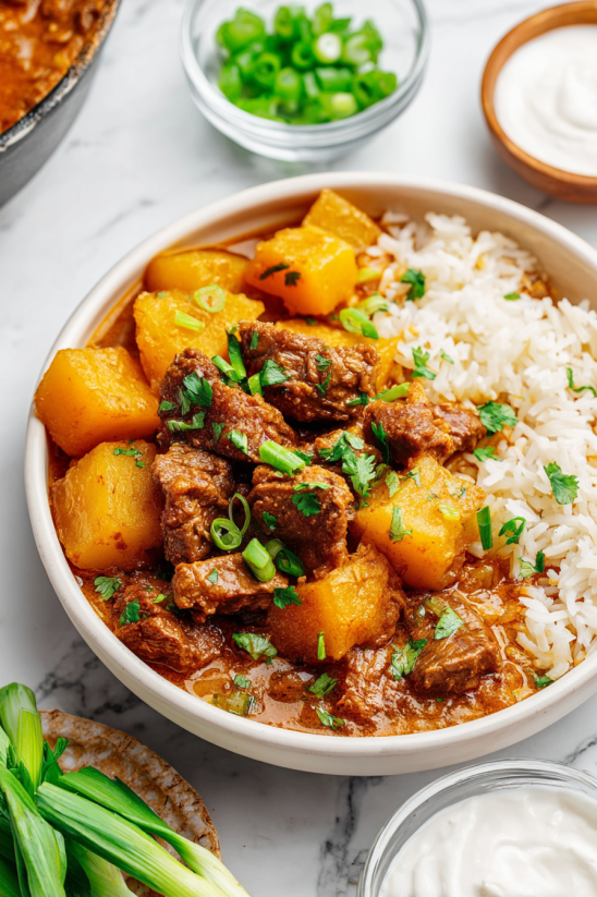 Ein weißer Teller mit einer mexikanischen Carne Guisada, die aus Rindfleisch, Kartoffeln, Zwiebeln und Tomaten zubereitet wurde.