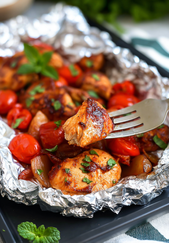 Ein Foil-Pack mit BBQ-Chicken, das mit Zwiebeln und Tomaten garniert ist.