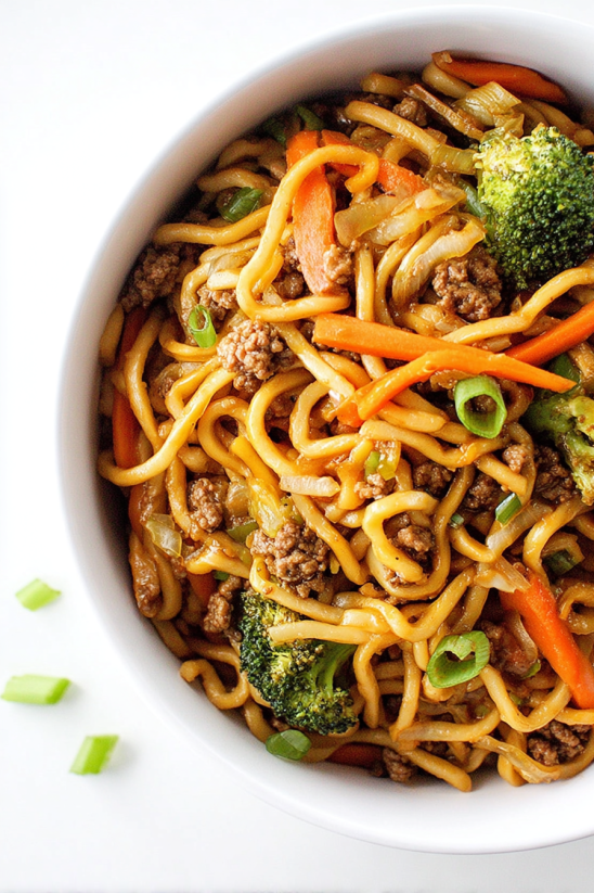 Ein weißer Teller mit einer Mischung aus Noodles, Karotten, Zwiebeln und Broccoli.