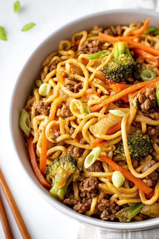 Ein weißer Teller mit einer Mischung aus Noodles, Meat und Gemüse, darunter Karotten und Broccoli.