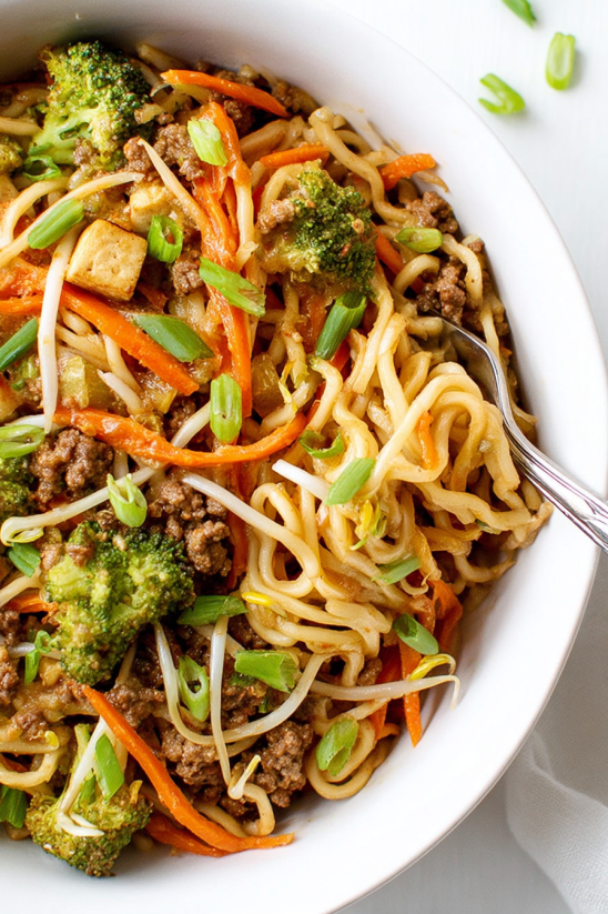 Ein Bogen chinesische Noodles mit vielen Zutaten wie Karotten, Broccoli, Rindfleisch und Koriander.