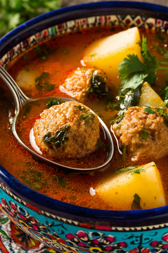 Ein Schalen mit Caldo de Albondigas (Mexican Meatball Soup) mit einer Garnitur aus Kartoffeln, Zwiebeln und Parsley.