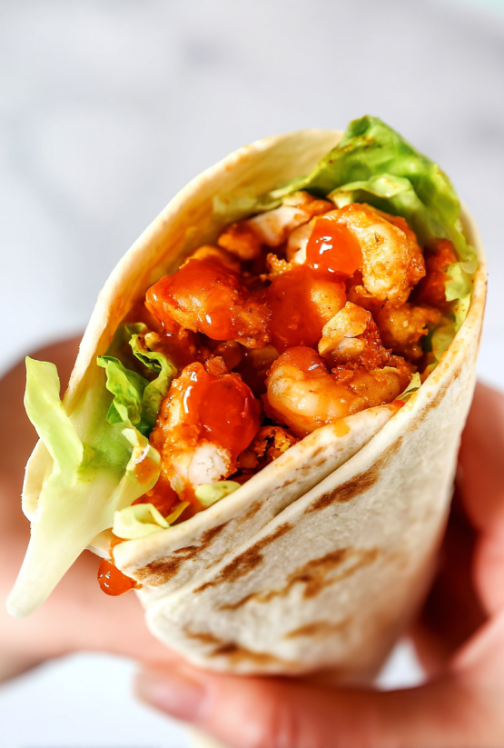 Ein Sticky Chicken Finger Wrap mit einer Kombination aus Käse, Chicken, Lettuce und Tomaten.