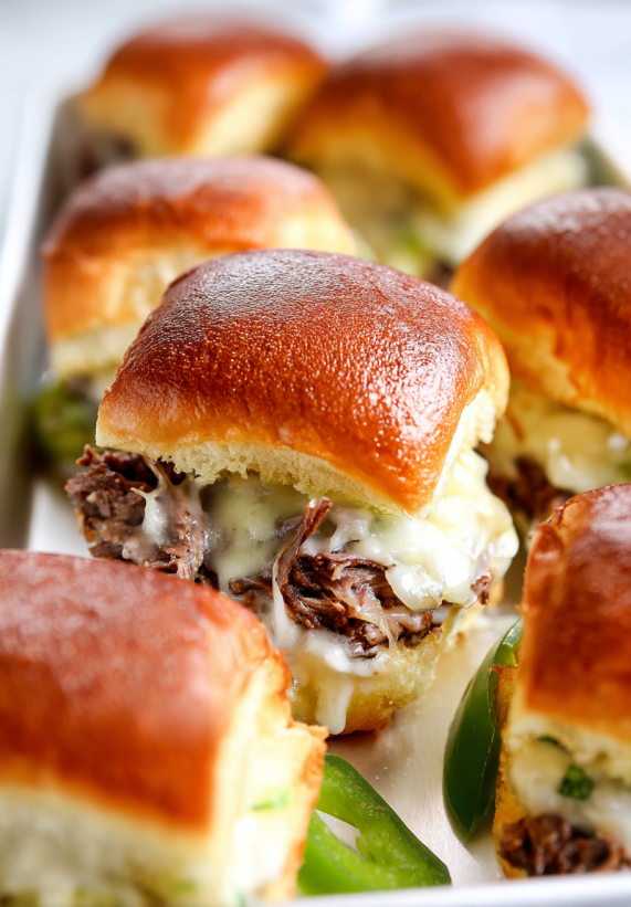 Eine Platte mit Cheesesteak Sliders, die aus Sandwiches bestehen, die mit Käse und Zwiebeln garniert sind.