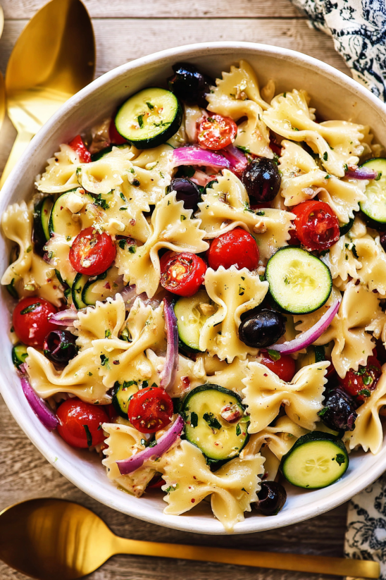 Ein weißer Becher mit einer Mischung aus Pasta, Zucchini, Tomaten, Basilikum und Oliven.
