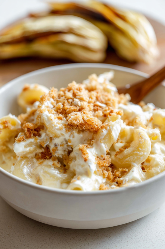 Ein weißer Teller mit Bananenpudding, der mit Nüssen und Zucker garniert ist.