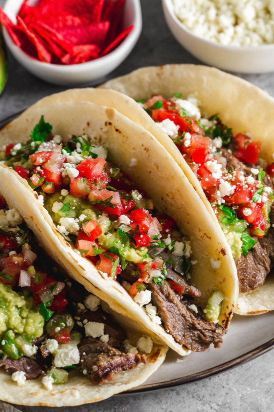 Zwei Flank Steak Tacos mit Tomaten, Basilikum und Mayonnaise auf einem Teller.