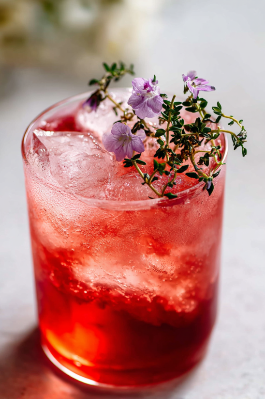 Ein Glas mit einem Transfusion Drink, der mit Eis und Blumen garniert ist.
