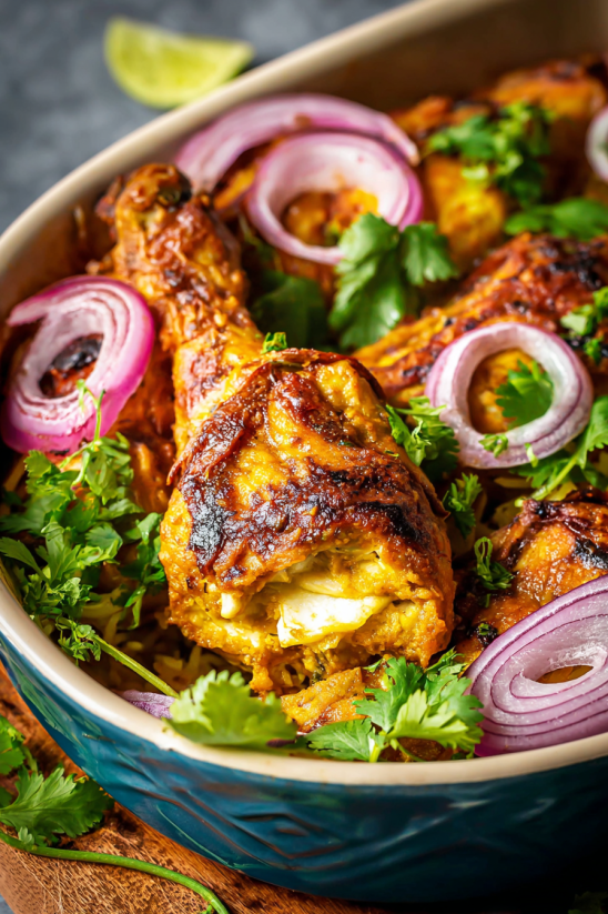 Ein indisches Tandoori Chicken in einem Behälter mit verschiedenen Zutaten wie Onions, Tomaten, Zwiebeln und Knoblauch.