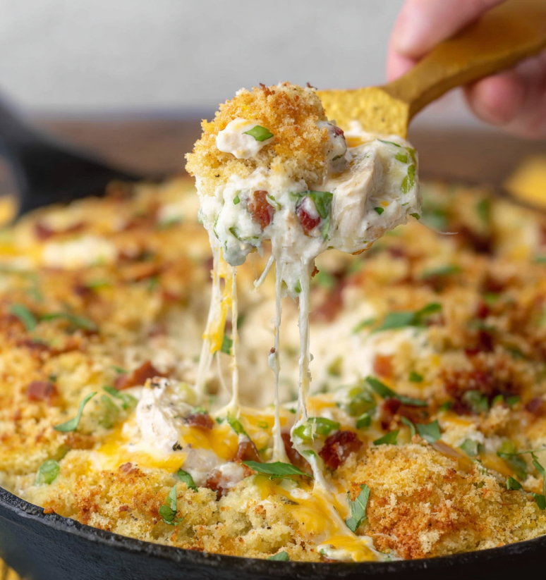 Ein Bacon Jalapeno Popper Dip wird aus einer Schüssel in einem schwarzen Teller gegeben.