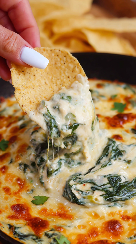 Eine Hand greift in ein Queso Spinach Dip und zieht es heraus.