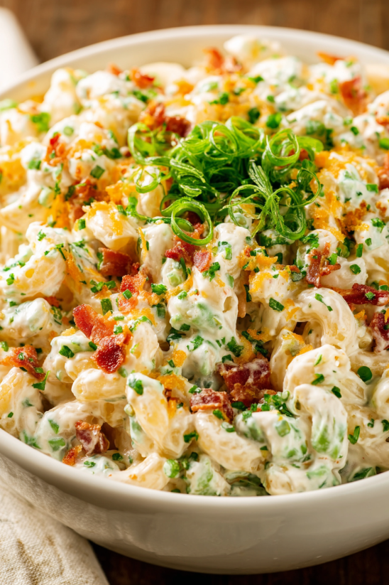 Ein Bild von Bacon Ranch Pasta Salad, das eine Mischung aus Pasta, Bacon, Zwiebeln und anderen Zutaten enthält.