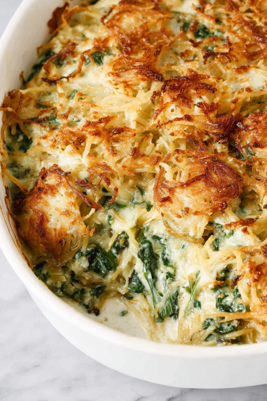 Ein Bild von einer Monterey Chicken Spaghetti Bake, die in einem weißen Behälter mit grünen Zutaten serviert wird.