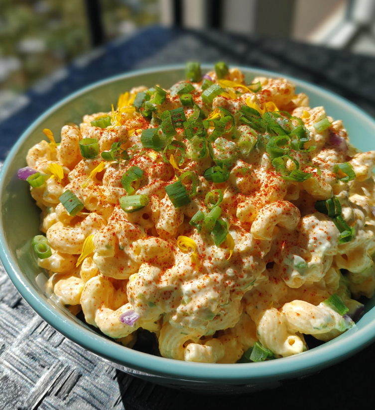 Ein blaues Bowl mit Macaroni Salat, der mit Zwiebeln und Paprika garniert ist.