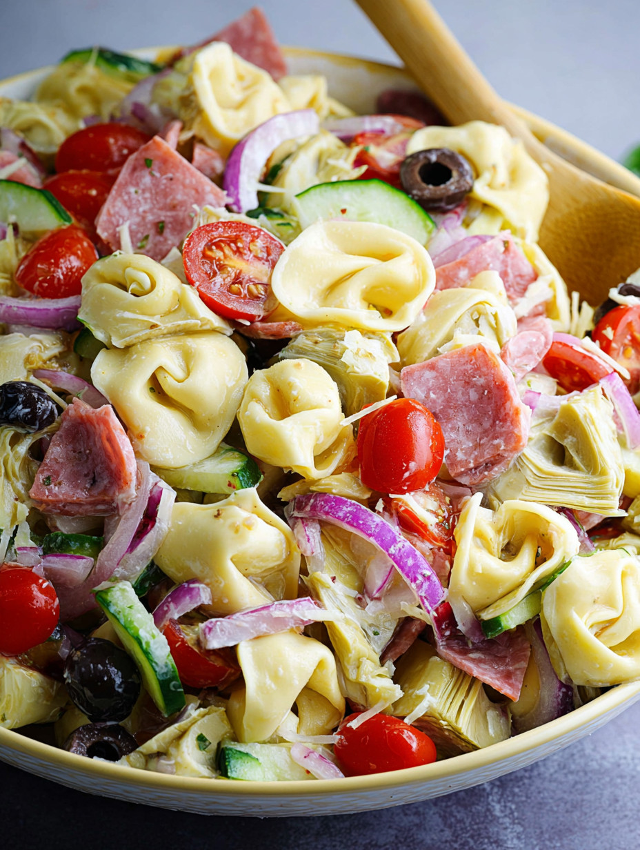 Eine Tortellini Pasta Salat mit Tomaten, Zwiebeln, Ham und Oliven.