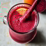 Ein Glas Beete-Orange-Smoothie mit einem Strohhalm.