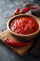 Eine kleine Schale mit roter Würzpaste und einer Chili oben drauf.